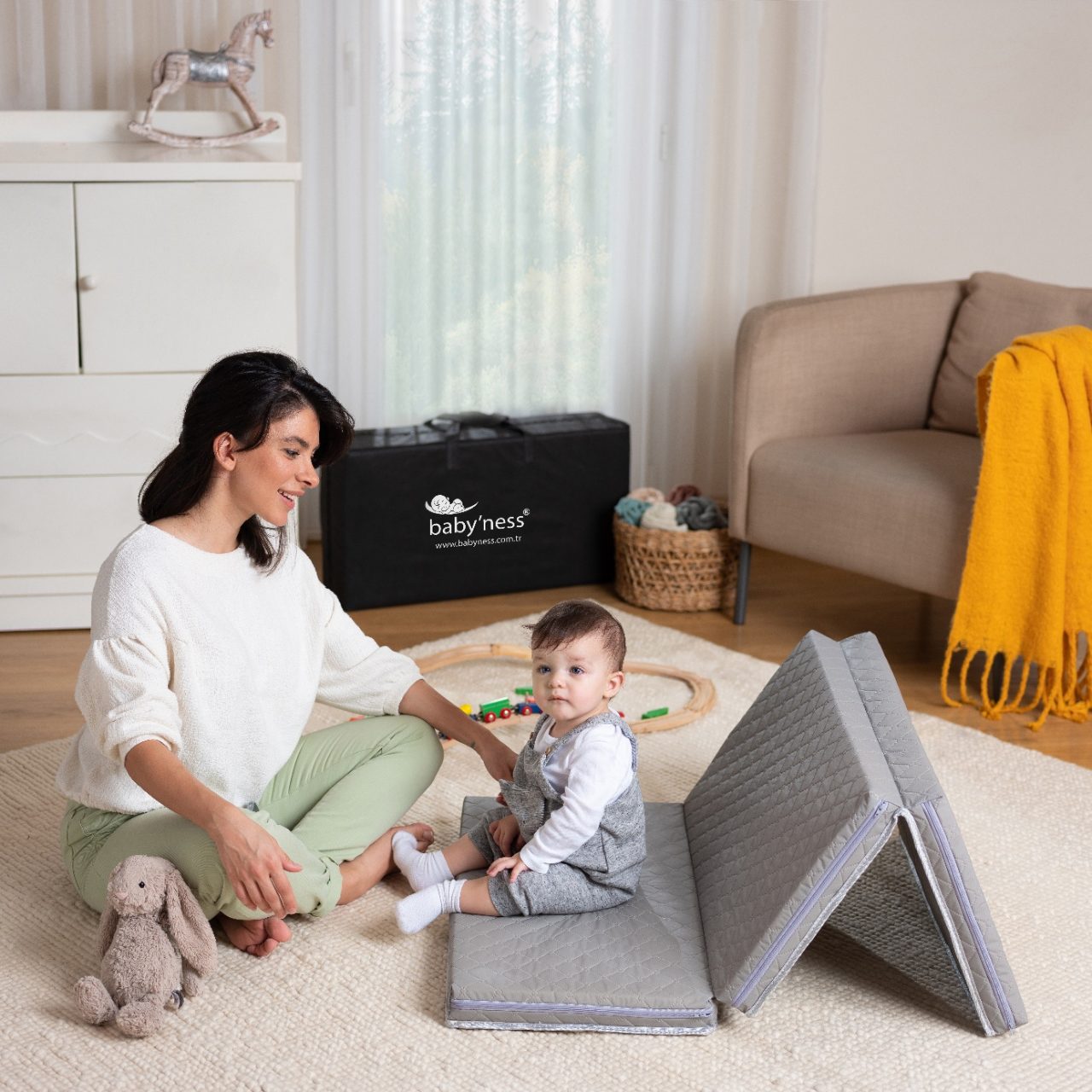 baby'ness grey folding baby mattress unfolded in a play area with its carry bag